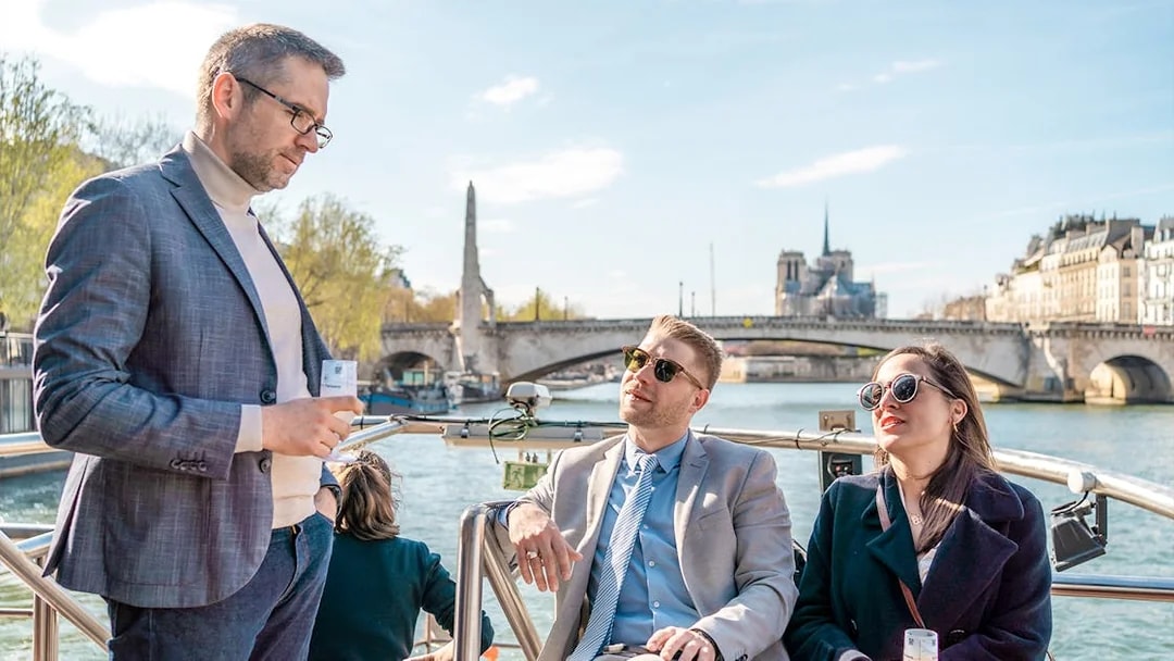 People enjoying champagne on a Seine River cruise with Notre-Dame in the background.