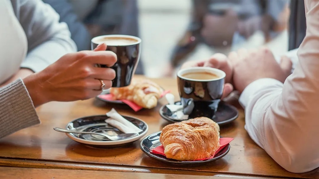 Two people enjoying coffee and croissants on a Seine River cruise in Paris.