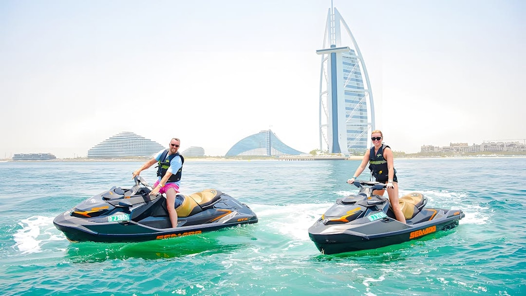 Two people jet skiing in Dubai with Burj Al Arab in the background.