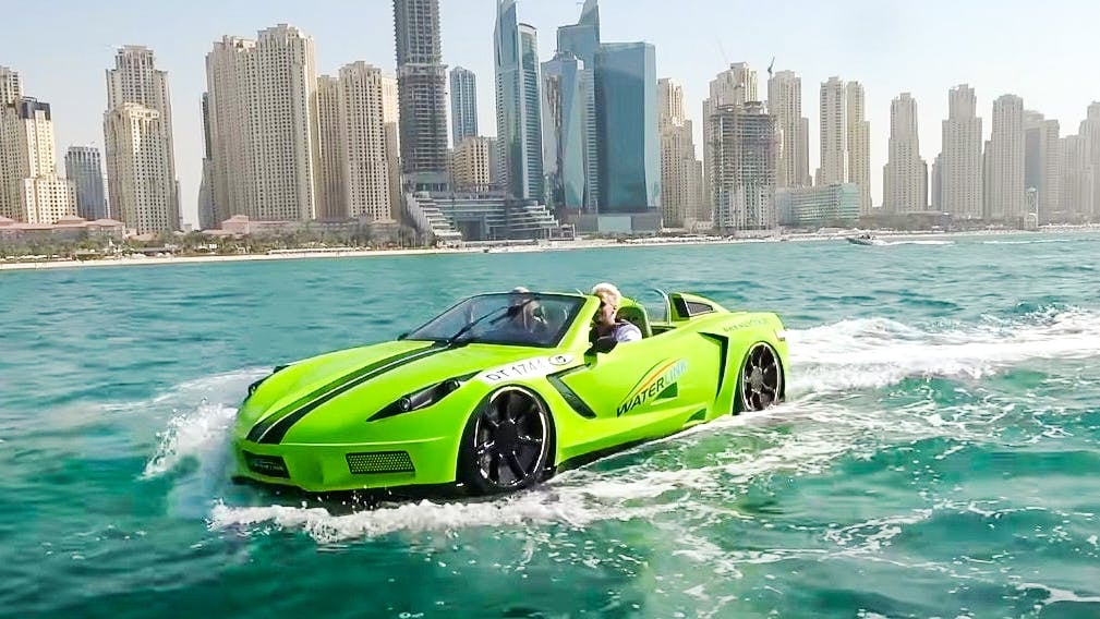 Man driving a green jet car corvette on water with Dubai skyline in the background.