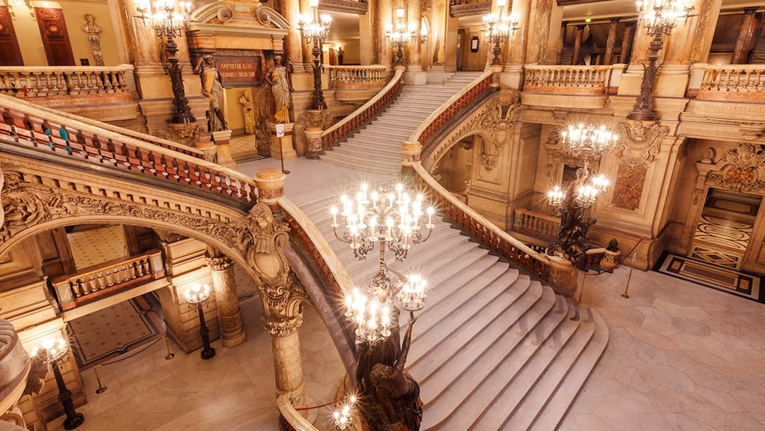 Opera Garnier's grand staircase with ornate chandeliers and intricate architectural details.
