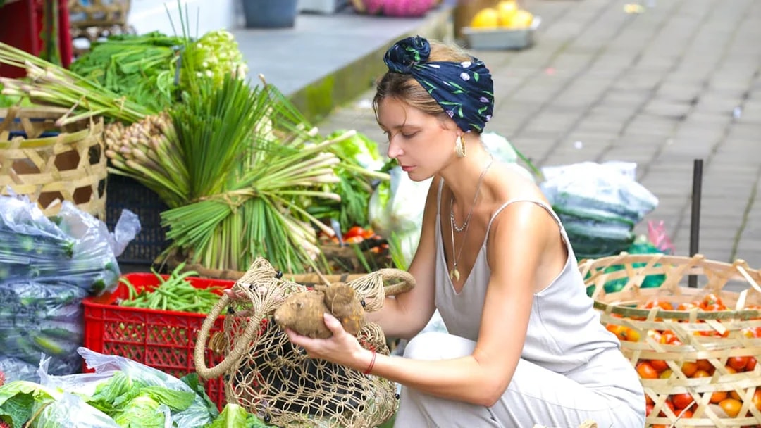 Woman selecting fresh produce at a Balinese market for Nia Balinese Cooking Class.