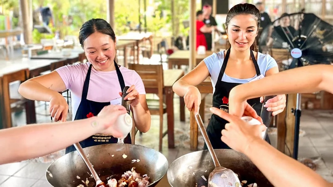 Participants cooking in a Nia Balinese cooking class, stirring ingredients in woks.