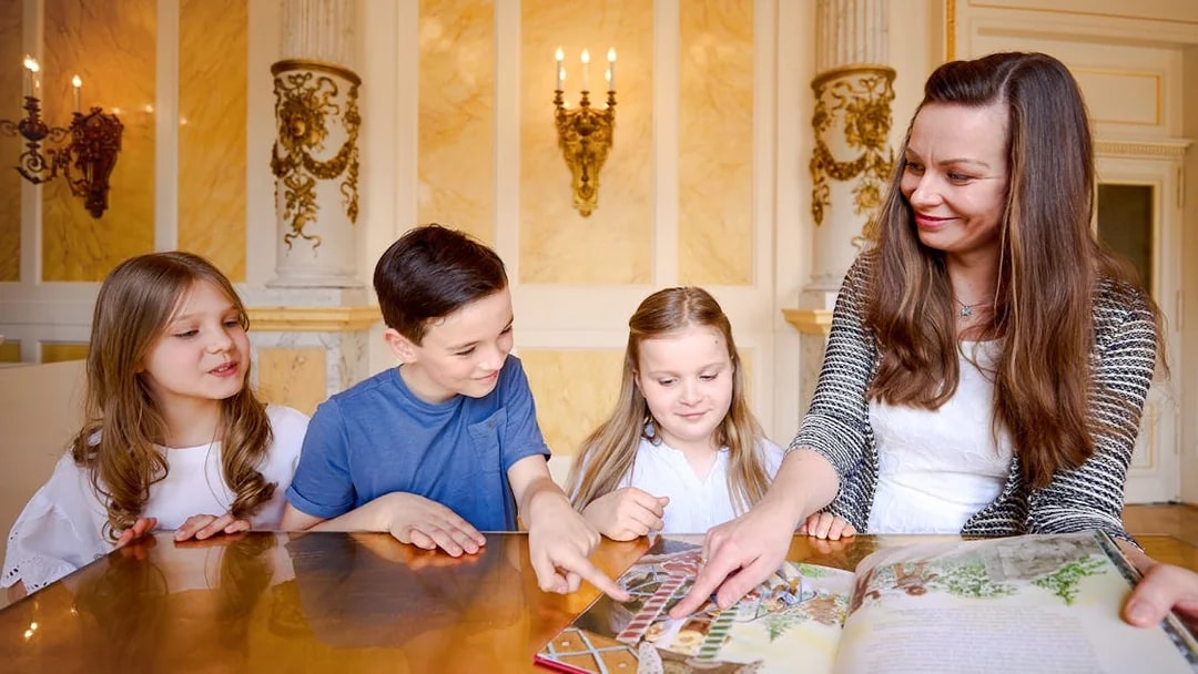 Guide showing children a book in an ornate room.