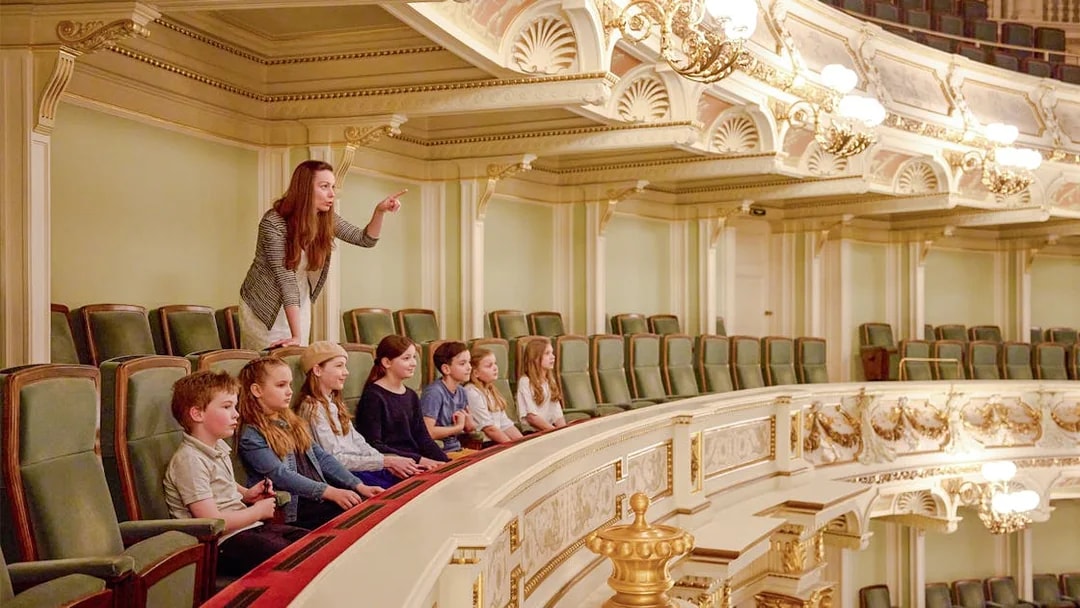Guide pointing out features to children in an ornate theater balcony.