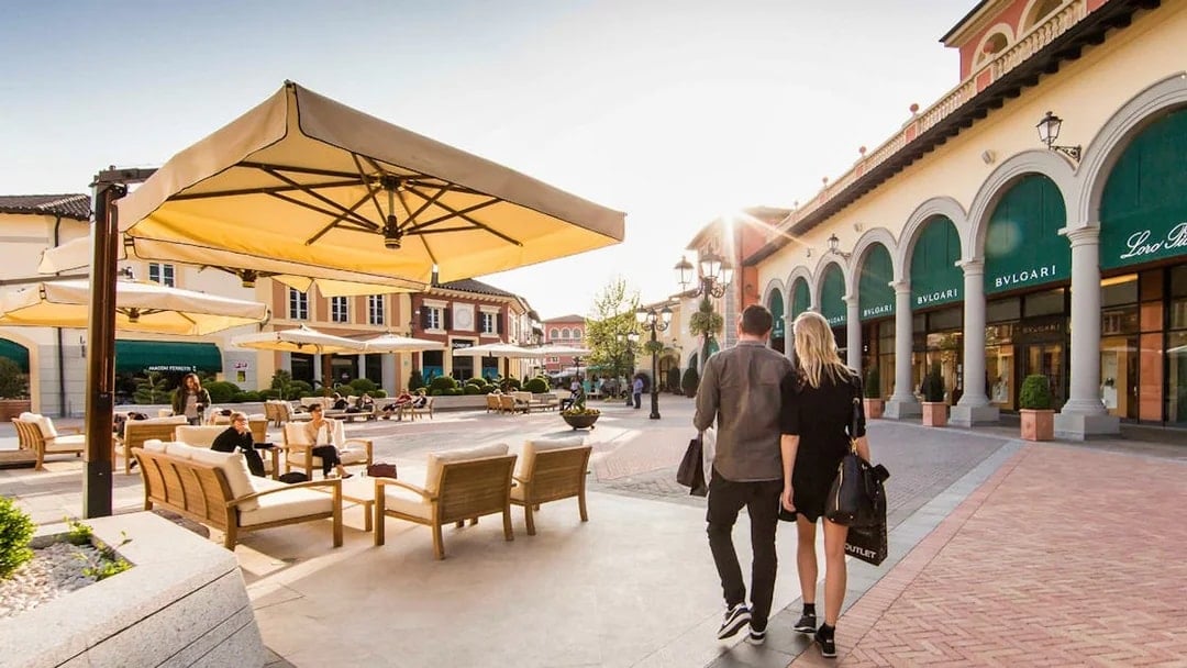 Couple walking at Serravalle Designer Outlet with shops and seating area.
