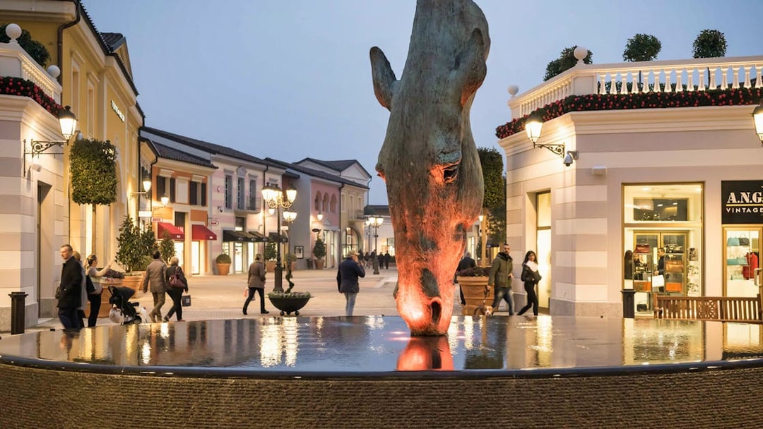 Serravalle Designer Outlet with horse sculpture and shoppers, transport from Milan.