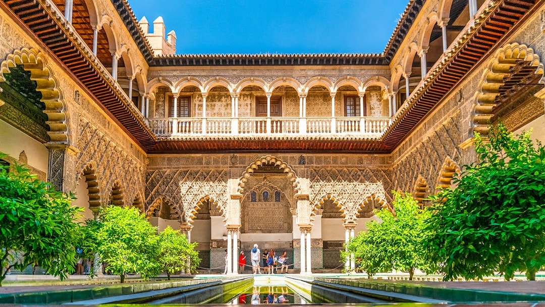 Tour group exploring Alcazar of Seville's Moorish architecture courtyard.