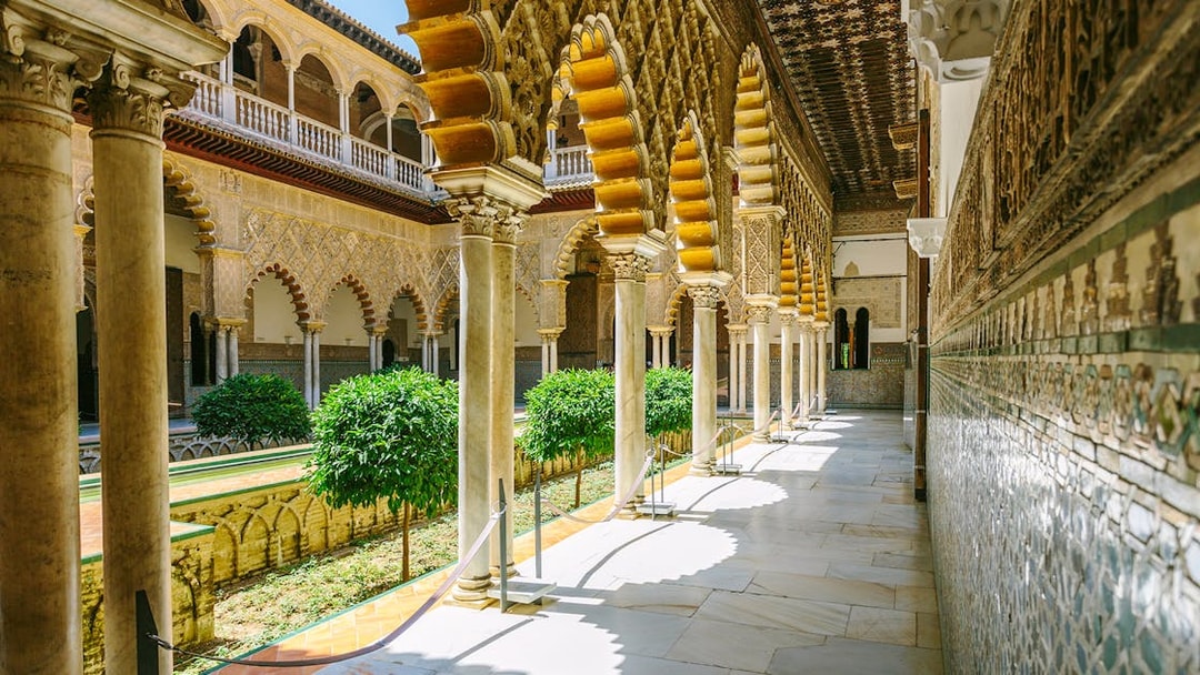 Alcazar of Seville courtyard with ornate arches and lush greenery.