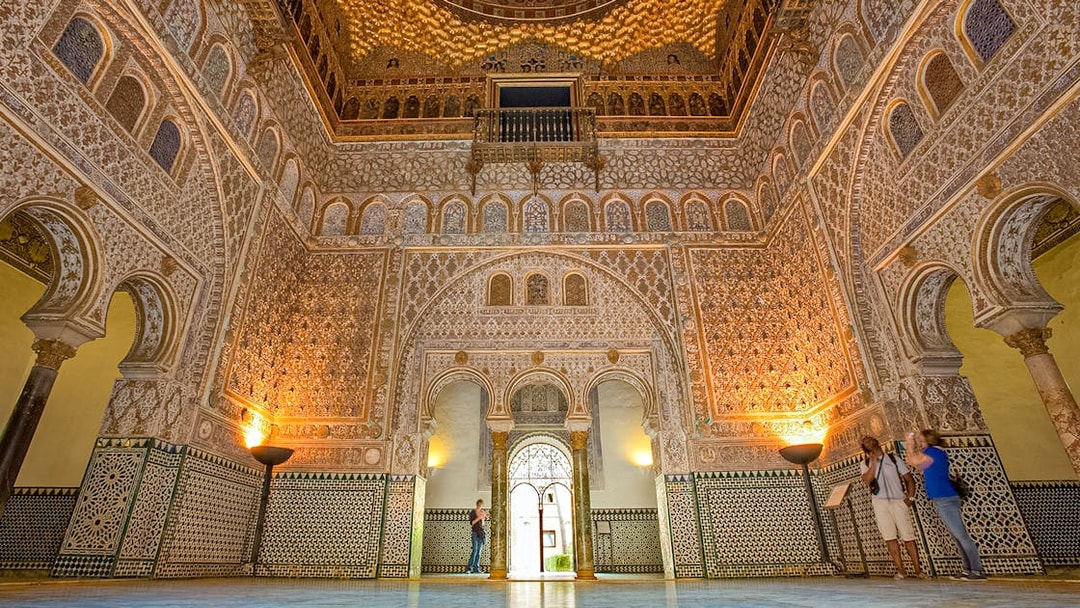 Ornate interior of the Alcazar of Seville with intricate tilework and arches.