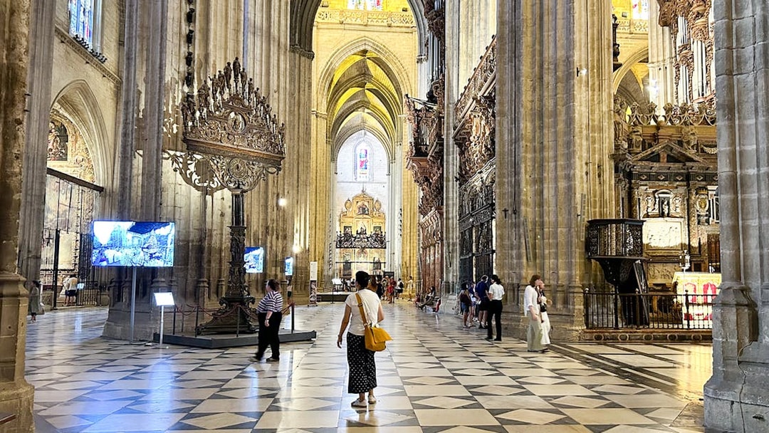 Interior of Seville Cathedral with visitors exploring the ornate architecture and high vaulted ceilings.
