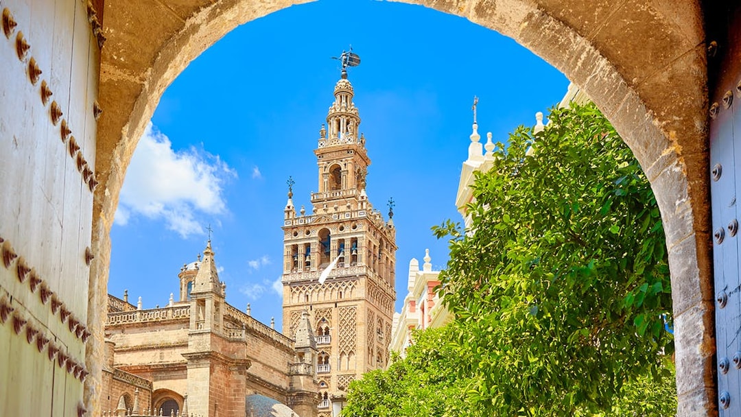 Seville's Giralda tower framed by an archway with clear blue sky.