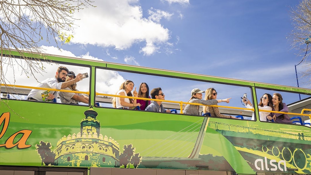 Tourists on Seville hop-on hop-off bus taking photos and enjoying city views.