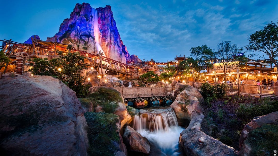 Shanghai Disney Adventure Isle with waterfall and illuminated rock formations at dusk.