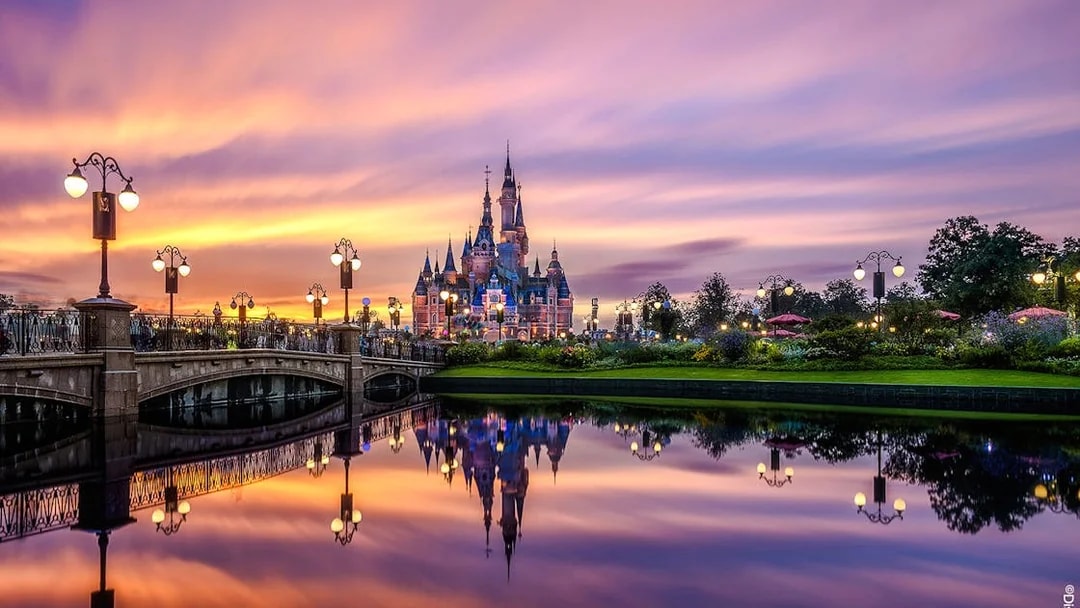 Shanghai Disney castle at sunset with reflections in the water.