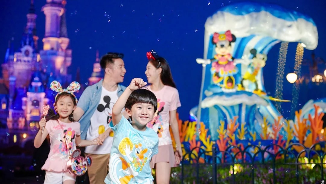 Family enjoying attractions at Shanghai Disneyland with castle and character statues in background.