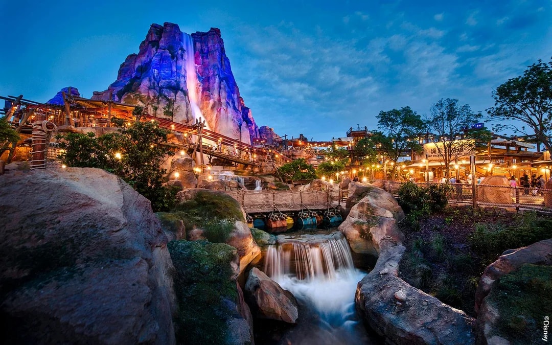 Shanghai Disney Adventure Isle with waterfall and illuminated rock formations at dusk.