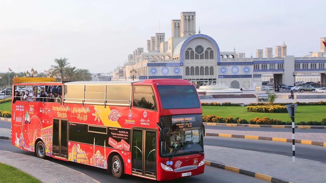 Red double-decker bus on Sharjah Hop-On-Hop-Off Tour passing Blue Souk.