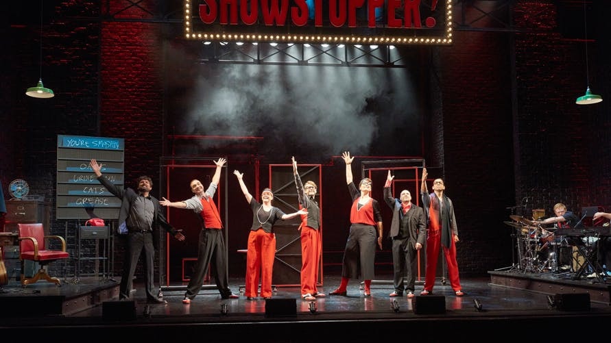 Performers on stage during Showstopper! The Improvised Musical, with arms raised in finale.