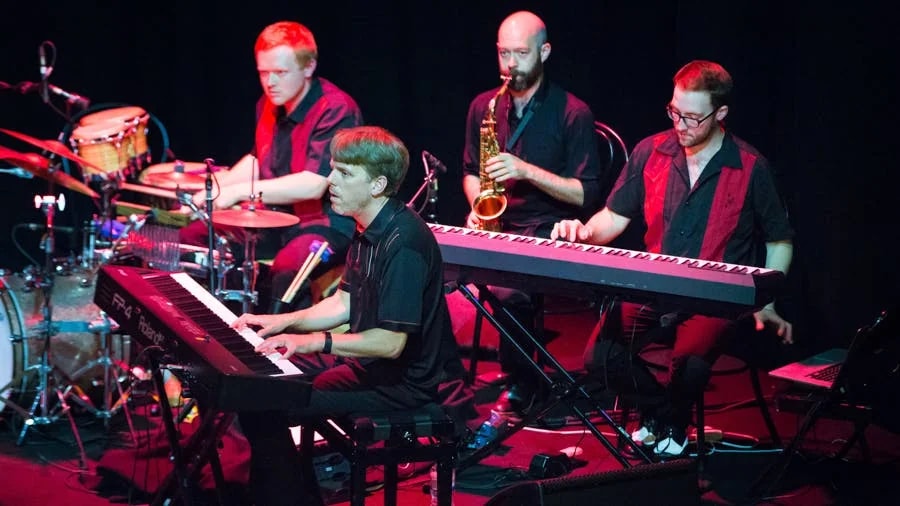 Musicians performing in Showstopper! The Improvised Musical with piano, saxophone, and drums.