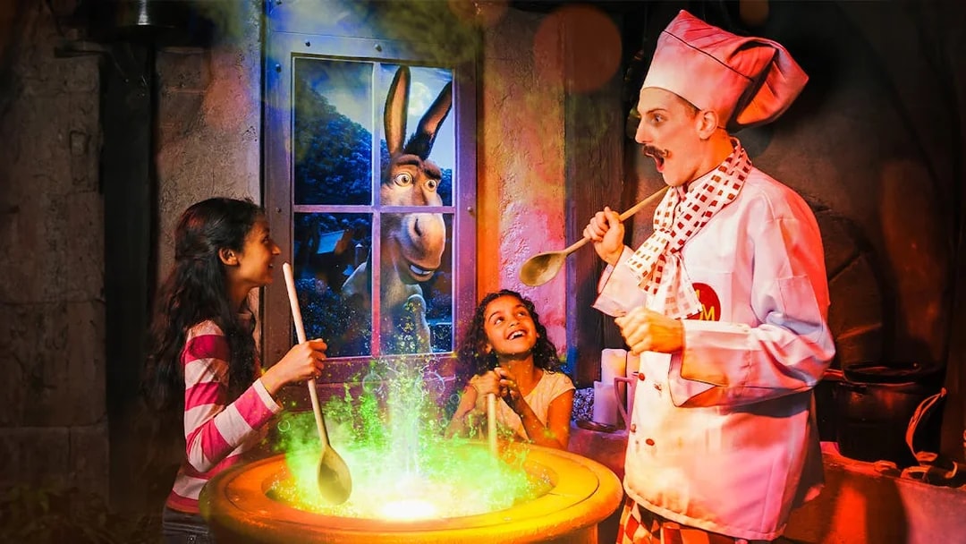 Children stirring a cauldron with a chef at Shrek’s Adventure! London, Donkey visible through window.