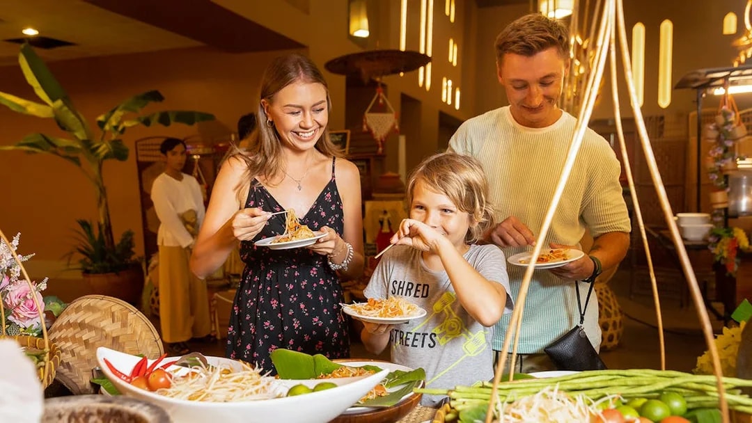 Family enjoying buffet dinner at Siam Niramit with plates of noodles and fresh vegetables.