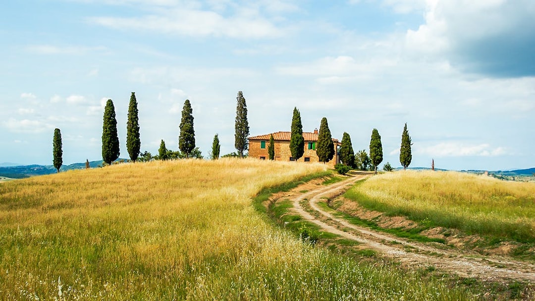 Tuscan countryside with a dirt path leading to a farmhouse near Siena, Italy.