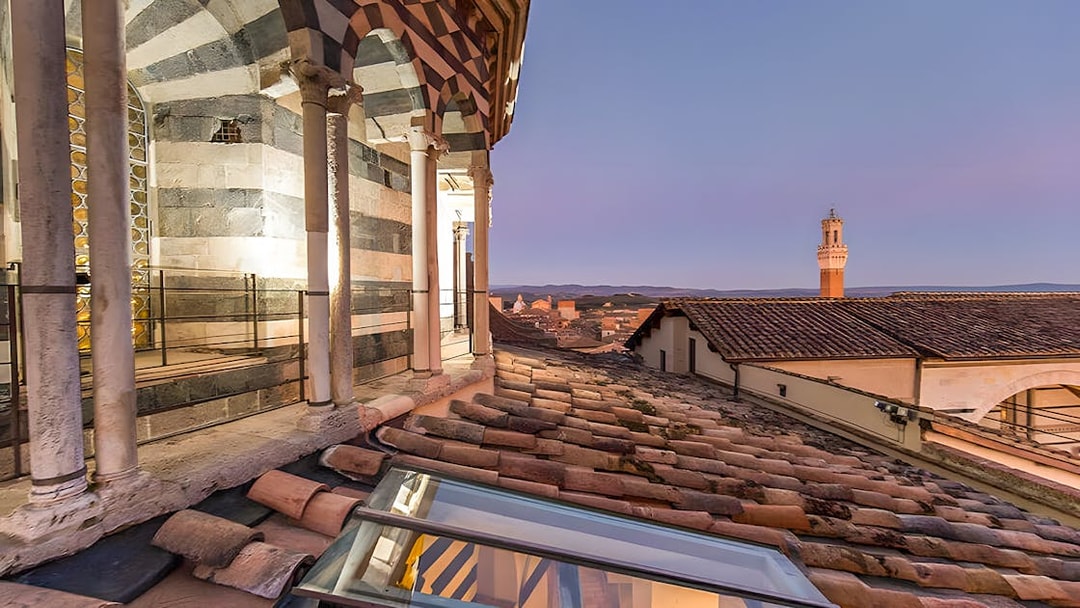 Siena Cathedral rooftop view at sunset, Italy, with cityscape in the background.