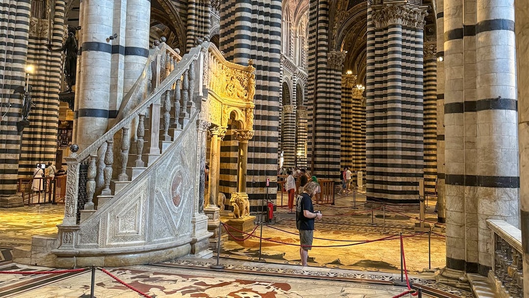 Siena Cathedral interior with striped columns and ornate staircase, Italy.