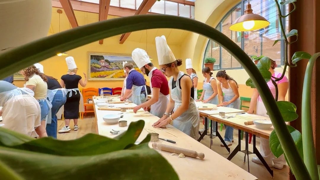 Participants in a cooking class in Siena preparing dough at a long table.