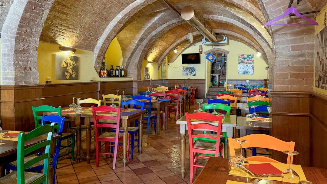 Colorful chairs and tables inside a brick-arched cafe in Siena for pasta cooking classes.