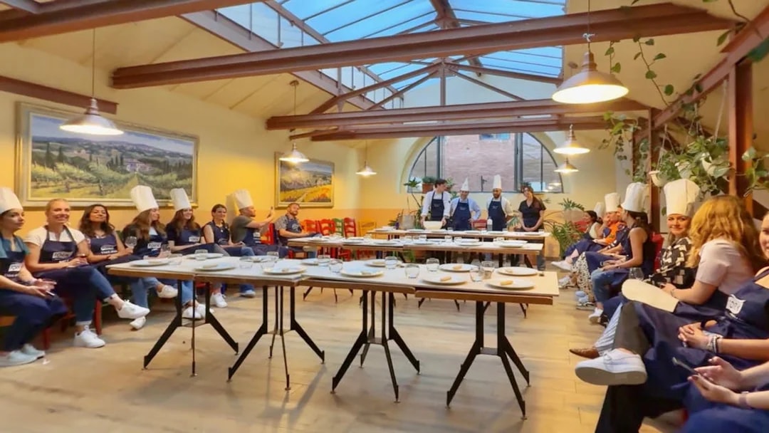 Participants in chef hats listening during a cooking class briefing in Siena.