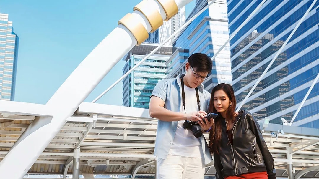 Couple using smartphone in Singapore city with modern architecture in background.