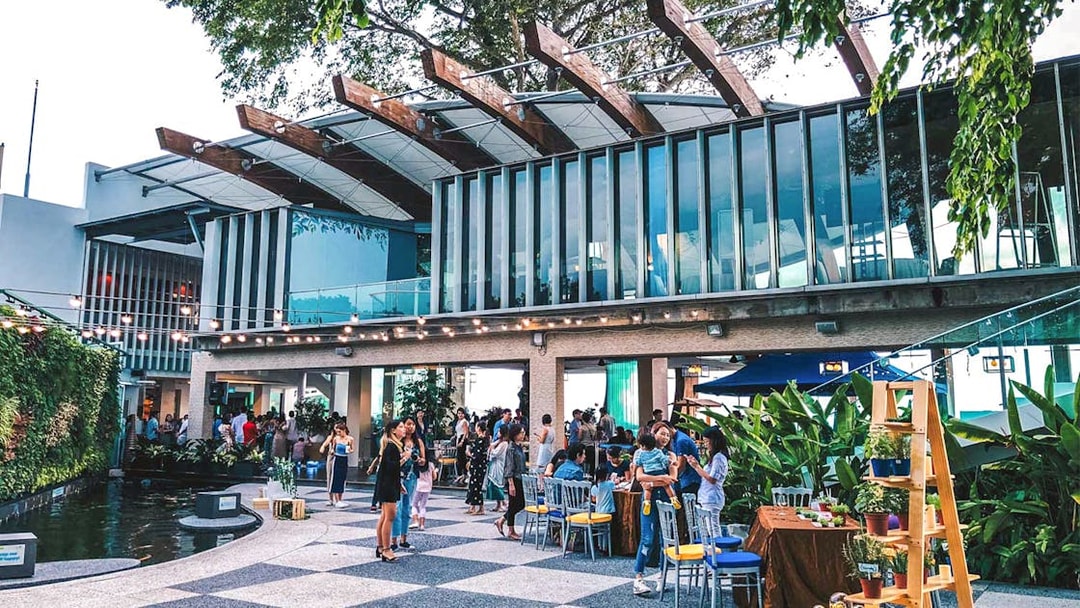 Outdoor gathering at a modern venue in Singapore with people socializing near greenery.