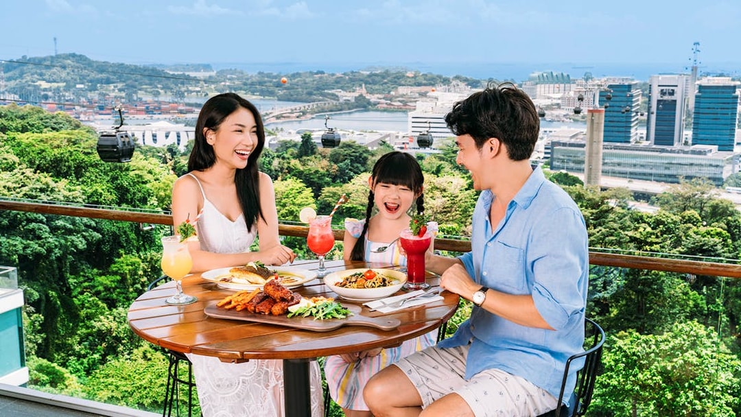 Tourists dining on Singapore Cable Car Sky Pass with city skyline view.