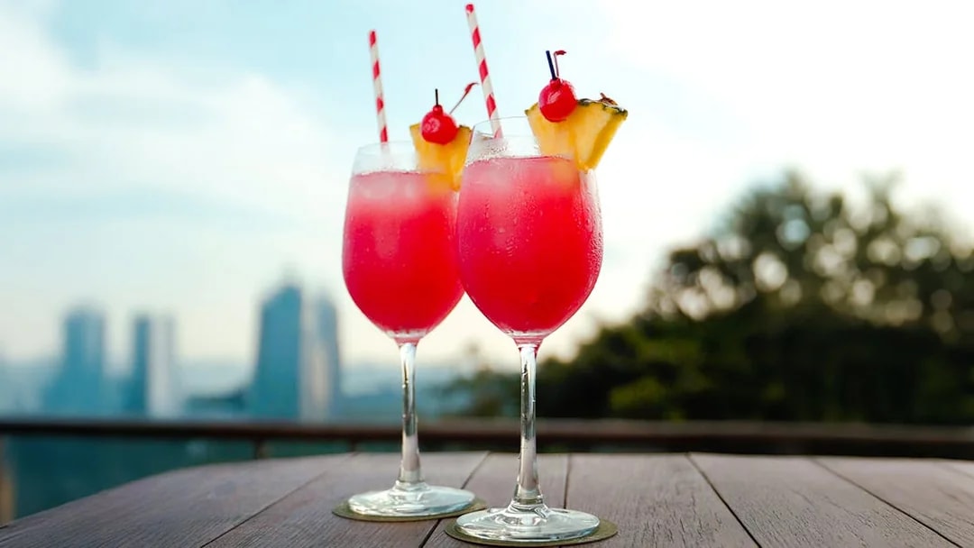 Two tropical cocktails on a table with a view of Singapore skyline.