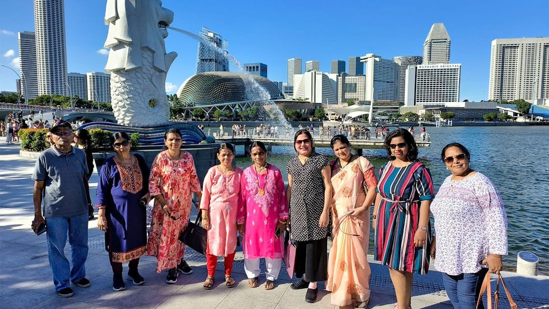 Group of tourists at Merlion Park with Singapore skyline in the background.