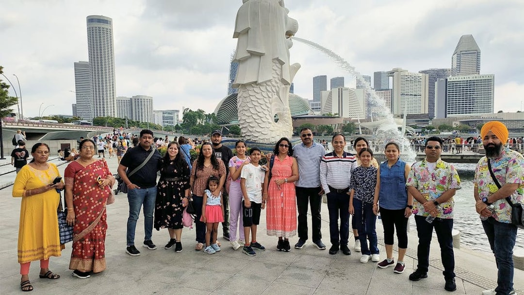 Group of tourists at Merlion Park with Singapore skyline in the background.