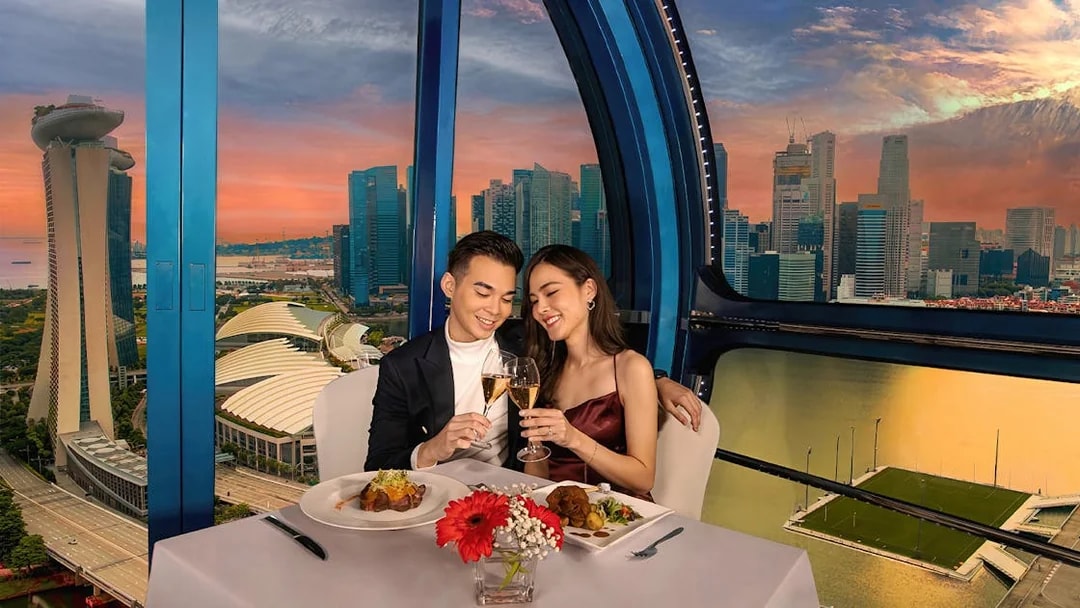 Couple toasting champagne at sunset on Singapore Flyer with city skyline view.