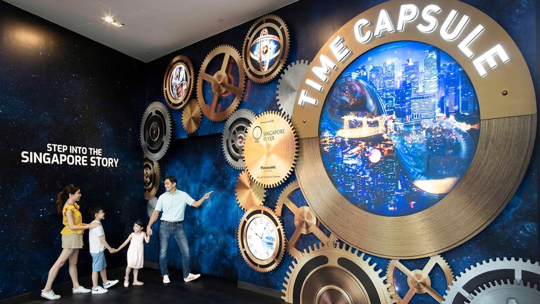 Family exploring Time Capsule exhibit at Singapore Flyer with cityscape display.
