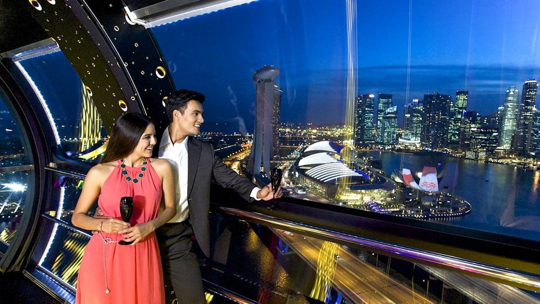 Couple enjoying drinks on Singapore Flyer with city skyline view during New Year's Eve countdown.