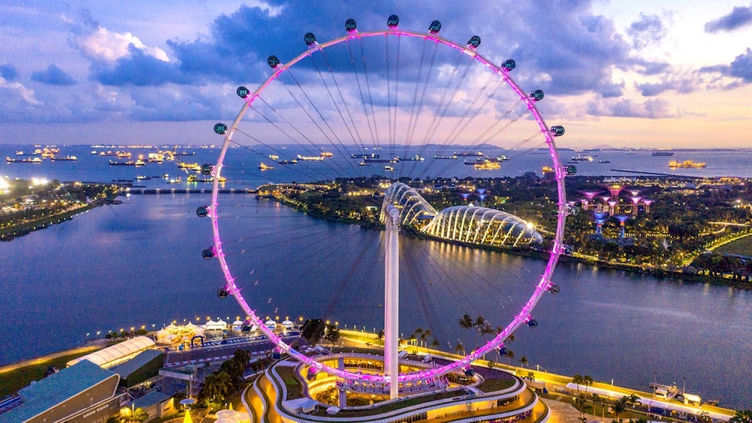 Aerial view of the illuminated Singapore Flyer at dusk with Marina Bay in the background.