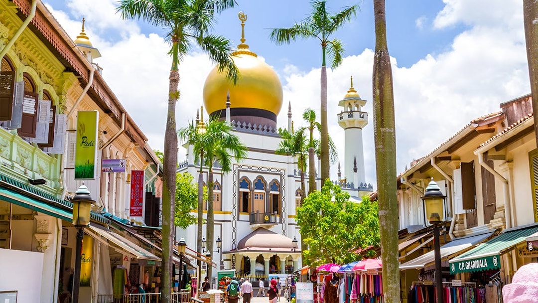 Sultan Mosque in Kampong Gelam, Singapore, with vibrant market stalls and palm trees.