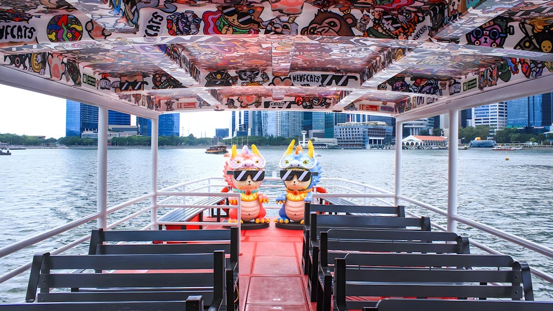 Colorful interior of a Singapore River Cruise boat by WaterB with city skyline in the background.