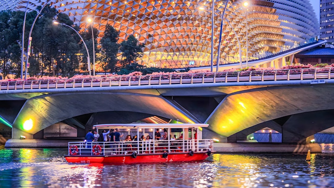 Singapore River Cruise boat passing under Esplanade Bridge at dusk.