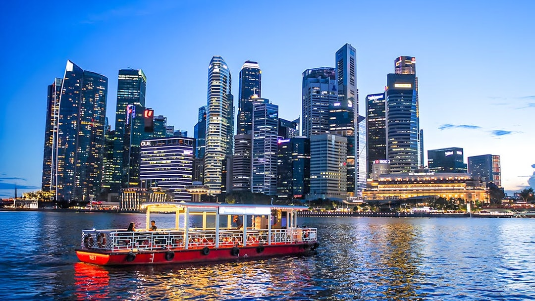 Singapore River Cruise boat on water with city skyline at dusk.