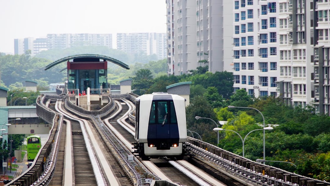 Singapore MRT train approaching a station, surrounded by residential buildings and greenery.