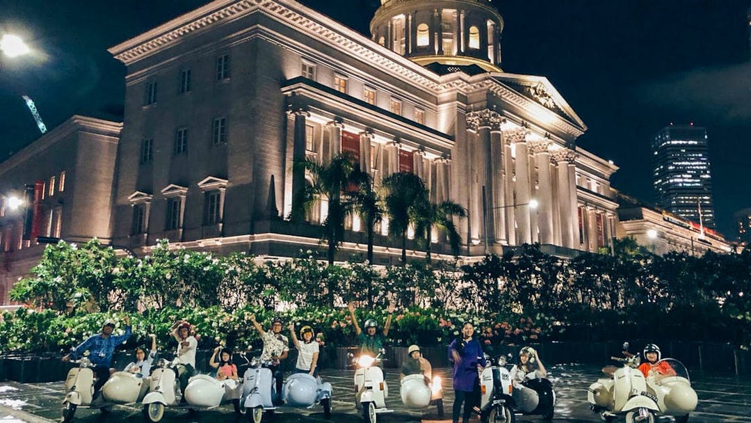 Tourists on vintage Vespa sidecars in front of Singapore's National Gallery at night.