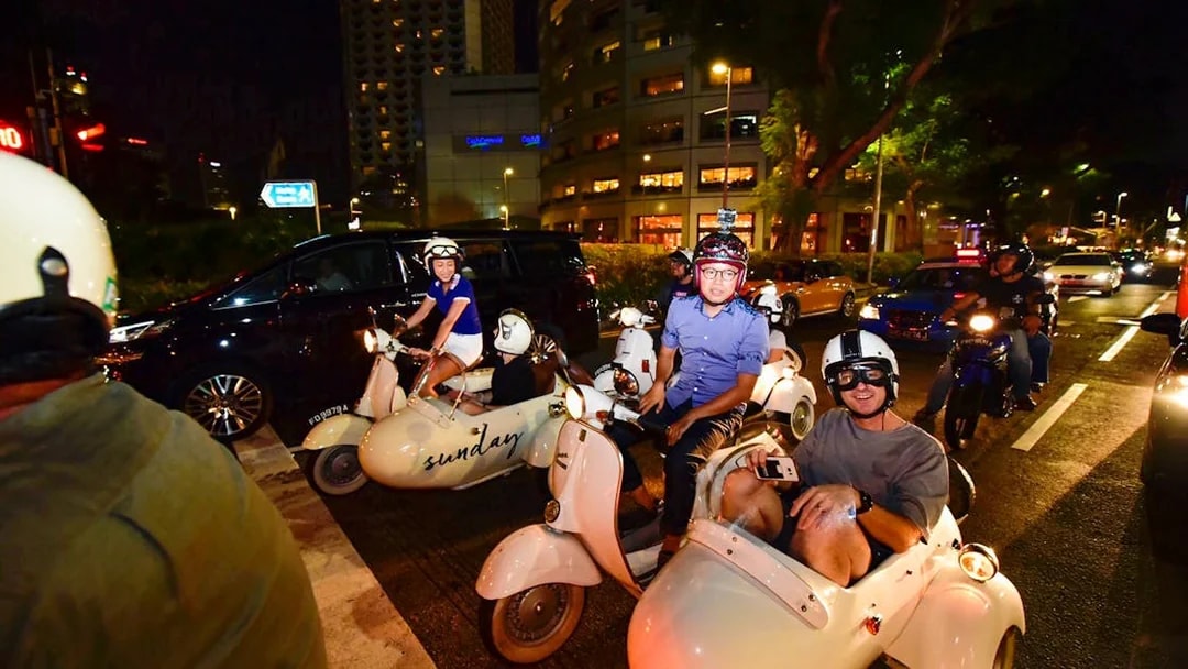 Vintage Vespa sidecars on a night tour in Singapore city streets.