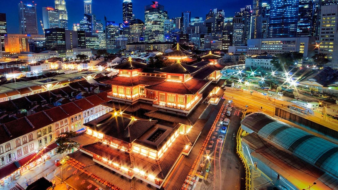 Buddha Tooth Relic Temple illuminated at night with Singapore skyline in the background.